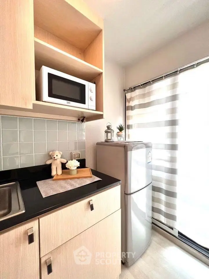 Modern kitchen with microwave, fridge, and stylish decor in bright apartment.