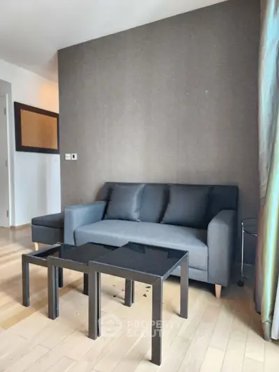 Modern living room with sleek gray sofa and minimalist black coffee tables on light wood flooring.