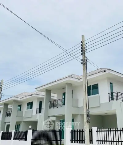 Modern two-story white houses with balconies and black railings under a clear sky.