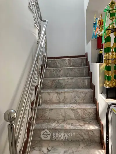 Elegant marble staircase with sleek metal railing and trophy display in a modern home.