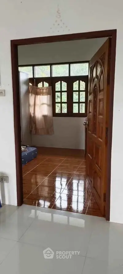 Charming bedroom with wooden door and tiled floor, featuring natural light from large windows.