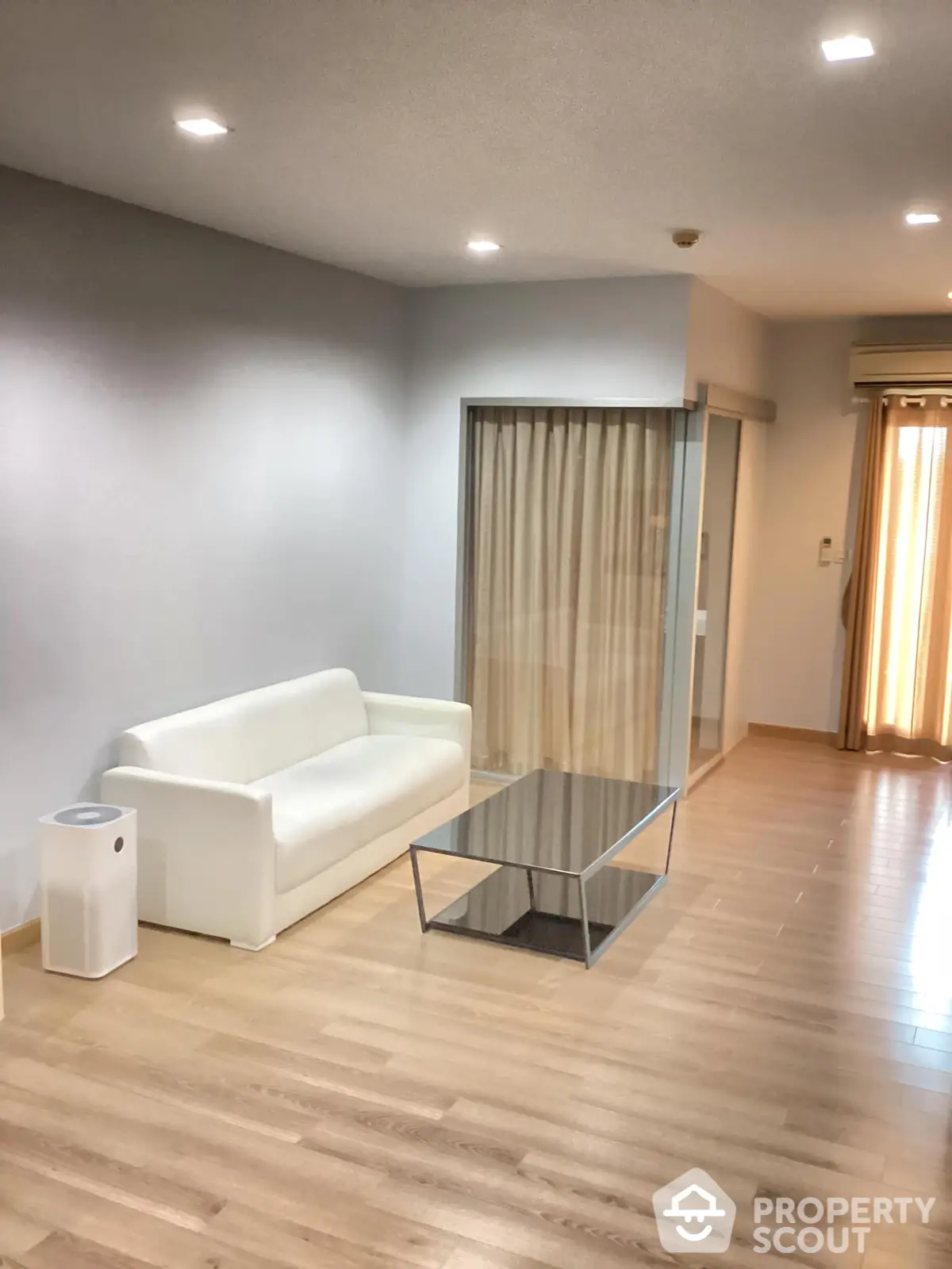 Spacious living room with gleaming hardwood floors, modern white sofa, and a sleek glass coffee table, bathed in natural light from large windows.