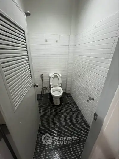Compact bathroom with modern white tiles and black flooring, featuring a standard toilet.