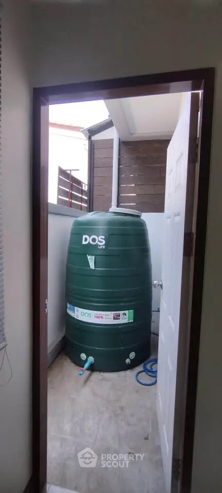 Compact storage room with large green water tank and tiled flooring.