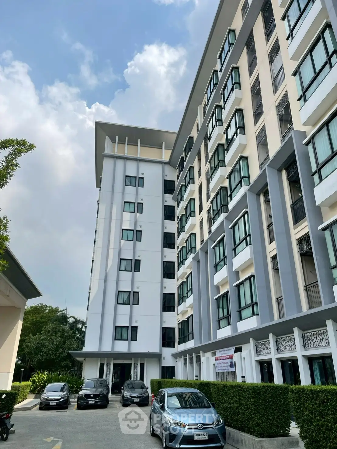 Modern multi-story residential building with parking and lush greenery.
