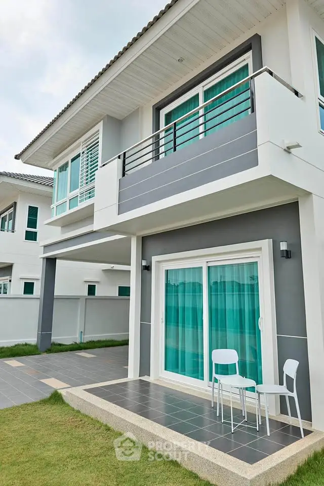 Modern two-story house with balcony and patio, featuring sleek design and large windows.