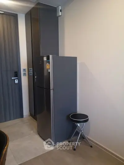 Modern kitchen corner with sleek fridge and folding stool in stylish apartment.