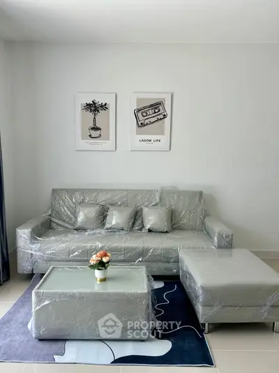 Modern living room with plastic-covered furniture and stylish wall art, featuring a cozy sofa and matching ottoman.