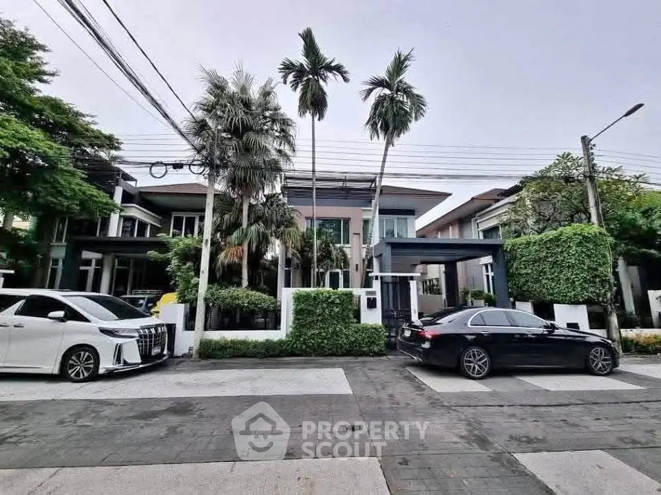 Modern luxury home with lush greenery and sleek cars in an upscale neighborhood.