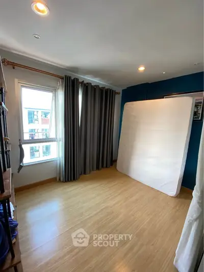 Spacious bedroom with wooden flooring and large window for natural light.