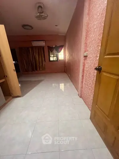 Spacious room with tiled flooring and vibrant pink walls, featuring a ceiling fan and air conditioning unit.