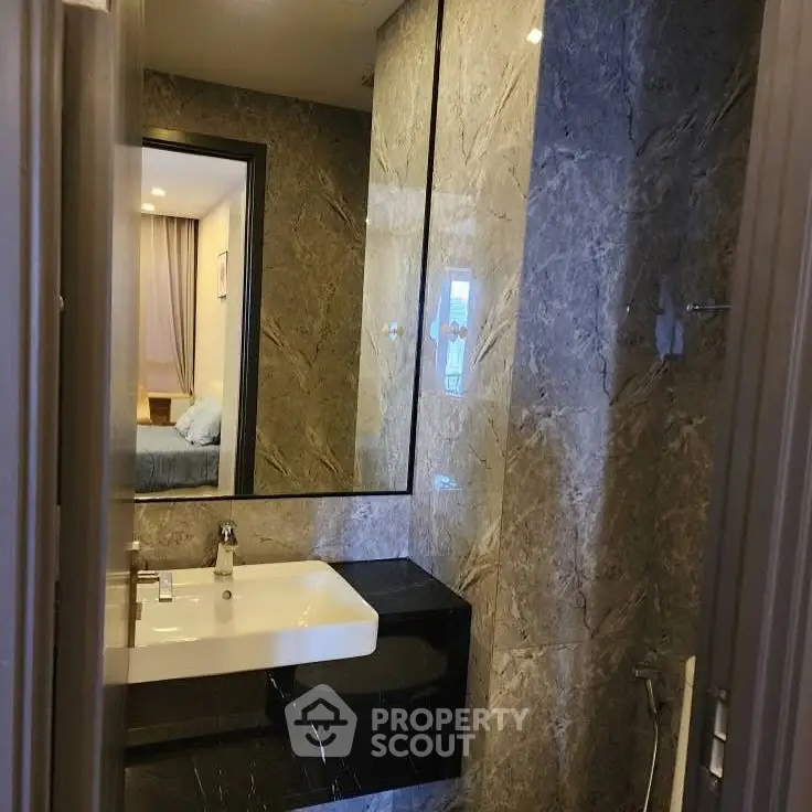 Luxurious marble bathroom with modern sink and mirror, adjacent to a cozy bedroom.