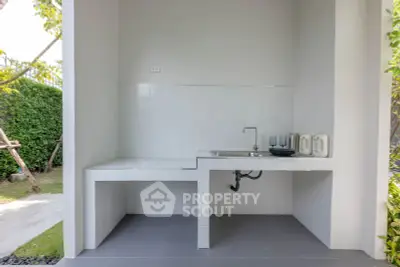 Modern outdoor kitchen with sleek white countertops and lush garden view.