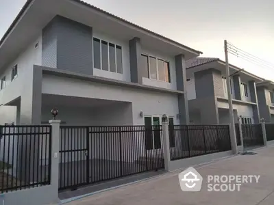 Modern two-story house with sleek design and gated driveway in suburban neighborhood.