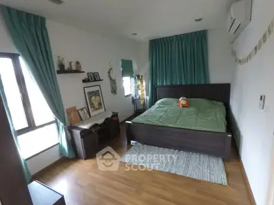 Cozy bedroom with wooden flooring and green accents, featuring a large window and modern decor.