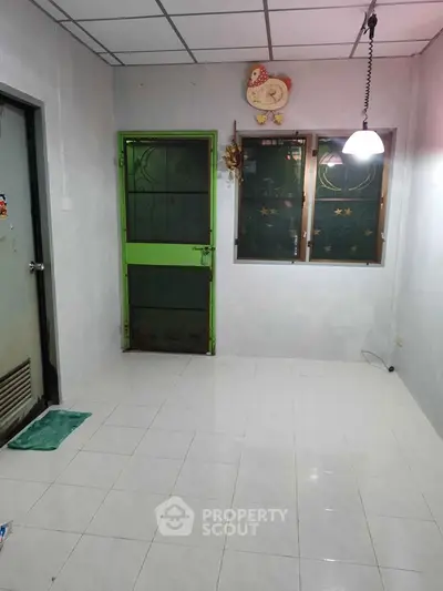 Minimalist room with tiled floor, green door, and hanging light fixture.