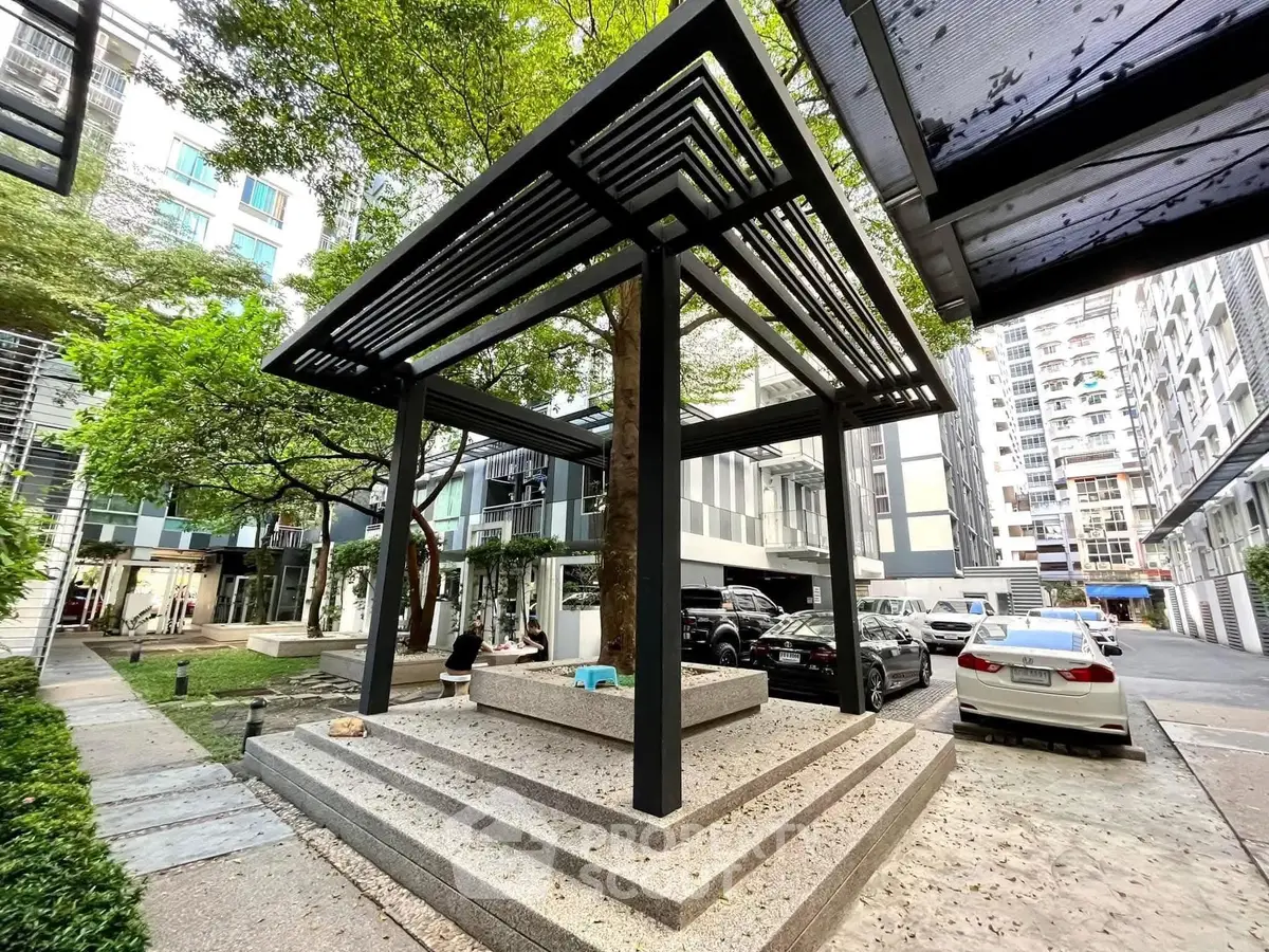 Modern urban courtyard with sleek pergola and parked cars in residential complex.