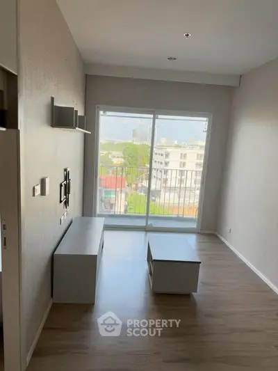 Modern living room with large window offering city view, featuring sleek furniture and wooden flooring.