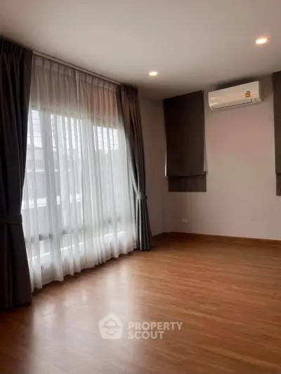 Spacious empty room with wooden flooring and large window, perfect for customization.
