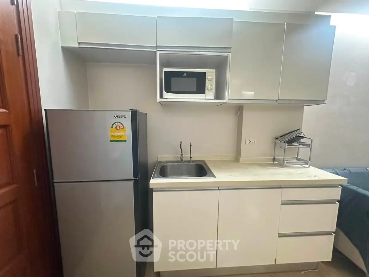 Modern kitchen with sleek cabinetry, stainless steel fridge, and built-in microwave in a compact layout.