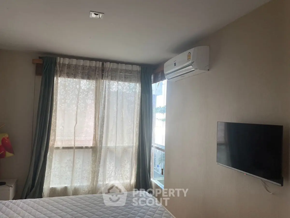 Cozy bedroom with natural light, featuring a wall-mounted TV and air conditioning unit.