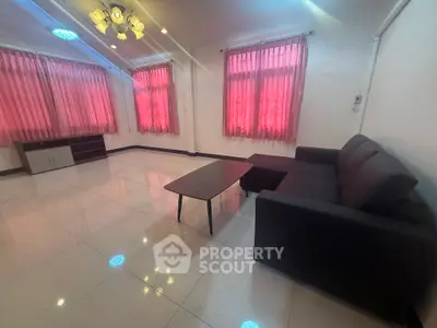 Spacious living room with modern sofa and coffee table, featuring large windows with pink curtains.