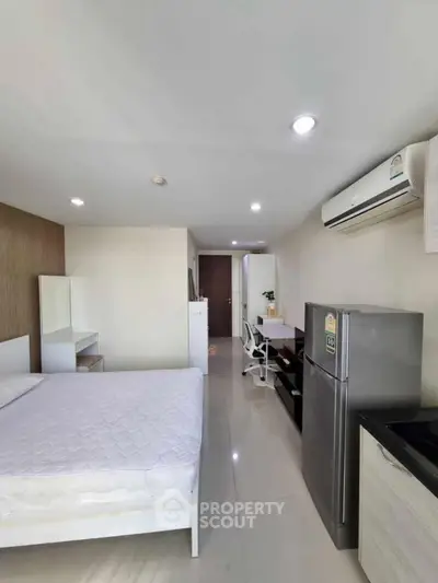 Modern studio apartment with sleek design, featuring a comfortable bed, air conditioning, and a compact kitchen area.