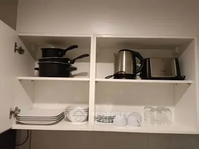 Modern kitchen cabinet with cookware, kettle, and toaster neatly arranged.
