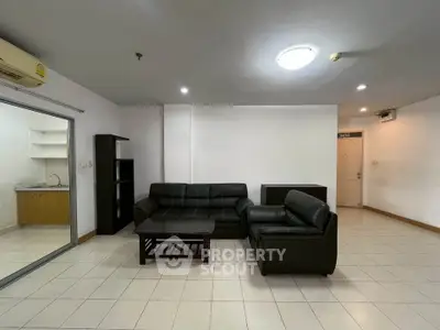 Spacious living room with modern black leather sofa and open layout kitchen in a contemporary apartment.