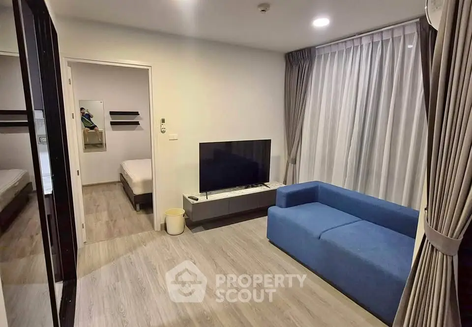 Modern living room with blue sofa and flat-screen TV, featuring elegant curtains and wooden flooring.