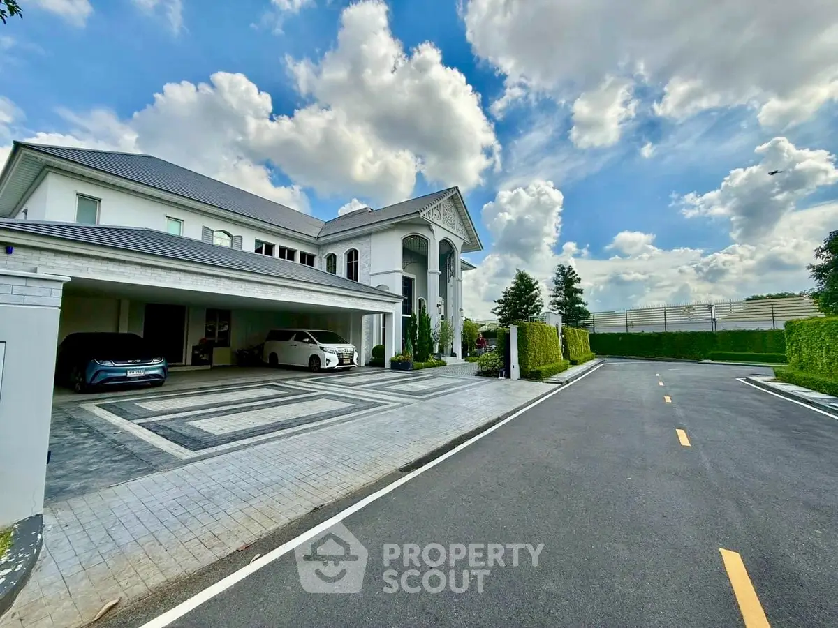 Luxurious mansion with expansive driveway and elegant architectural design under a bright blue sky.