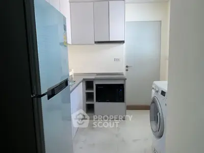 Modern kitchen with sleek appliances including fridge, microwave, and washing machine in compact layout.