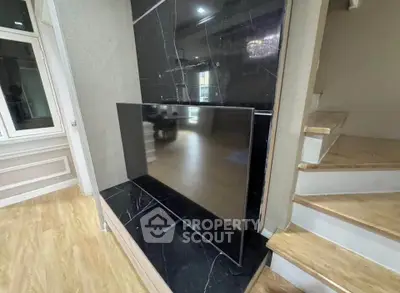 Modern living room with sleek black marble TV wall and wooden staircase