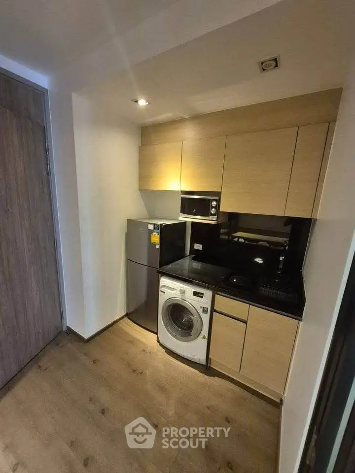 Modern compact kitchen with appliances including fridge, microwave, and washing machine.