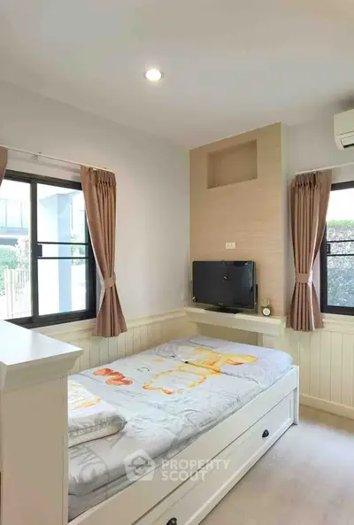 Cozy bedroom with natural light and modern decor, featuring a built-in TV and stylish curtains.