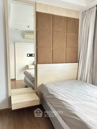 Modern bedroom with stylish headboard and large mirror, featuring elegant curtains and wooden flooring.