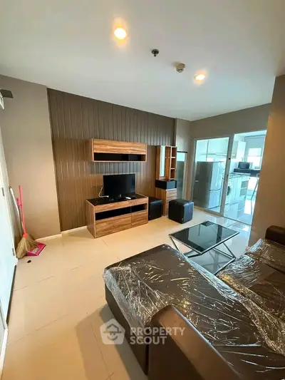 Modern living room with sleek furniture and glass partition leading to kitchen area.