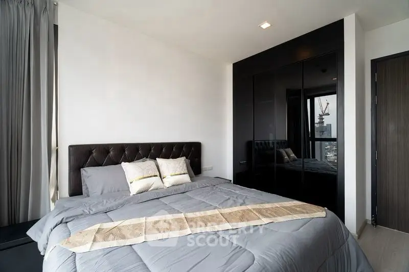 Modern bedroom with sleek black wardrobe and city view window, featuring a cozy bed with elegant decor.