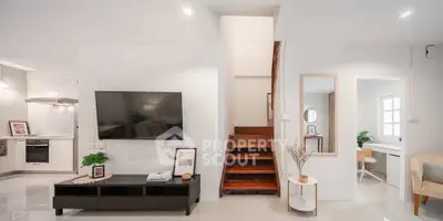 Modern living room with sleek TV setup and stylish staircase in bright, open-concept home.