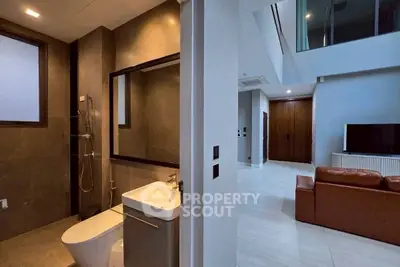 Modern interior with sleek bathroom and spacious living area featuring a leather sofa and large TV.