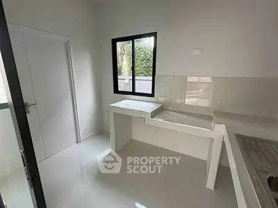 Modern minimalist kitchen with sleek white countertops and large window