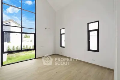 Spacious modern room with large windows and wooden flooring, offering abundant natural light and garden view.