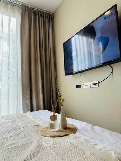 Cozy bedroom with wall-mounted TV and elegant decor, featuring a large window with curtains.