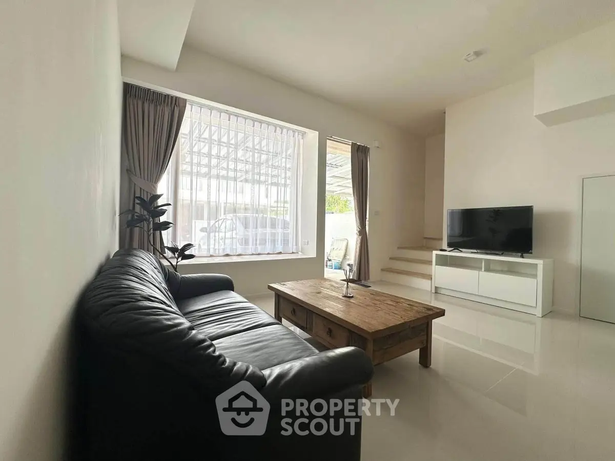 Spacious living room with modern decor, featuring a sleek black sofa, wooden coffee table, and large window.