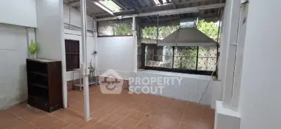 Spacious semi-outdoor kitchen with tiled flooring and large ventilation hood.