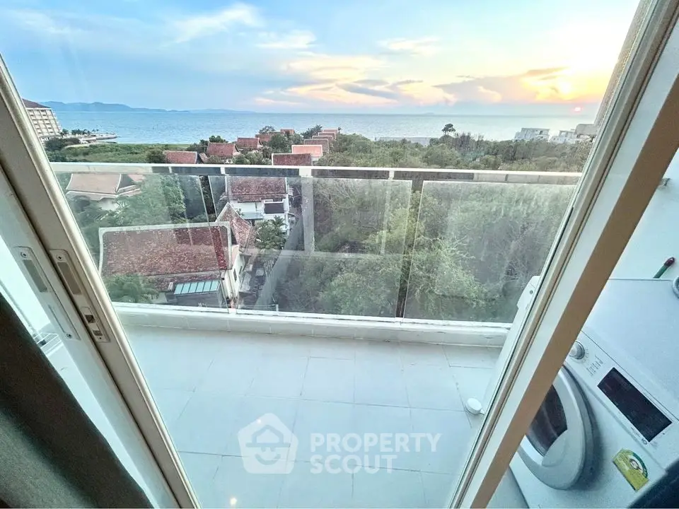 Stunning balcony view with ocean and sunset, featuring modern glass railing and washing machine.