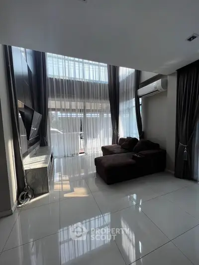 Spacious modern living room with high ceilings and large windows, featuring a cozy sofa and sleek TV setup.