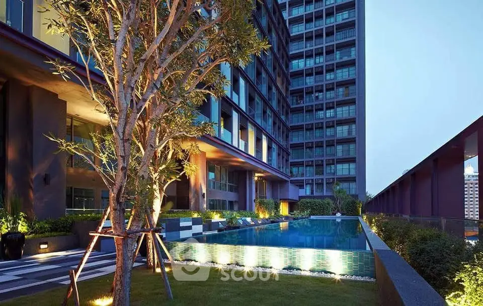 Luxurious modern apartment building with illuminated pool and lush greenery at dusk.