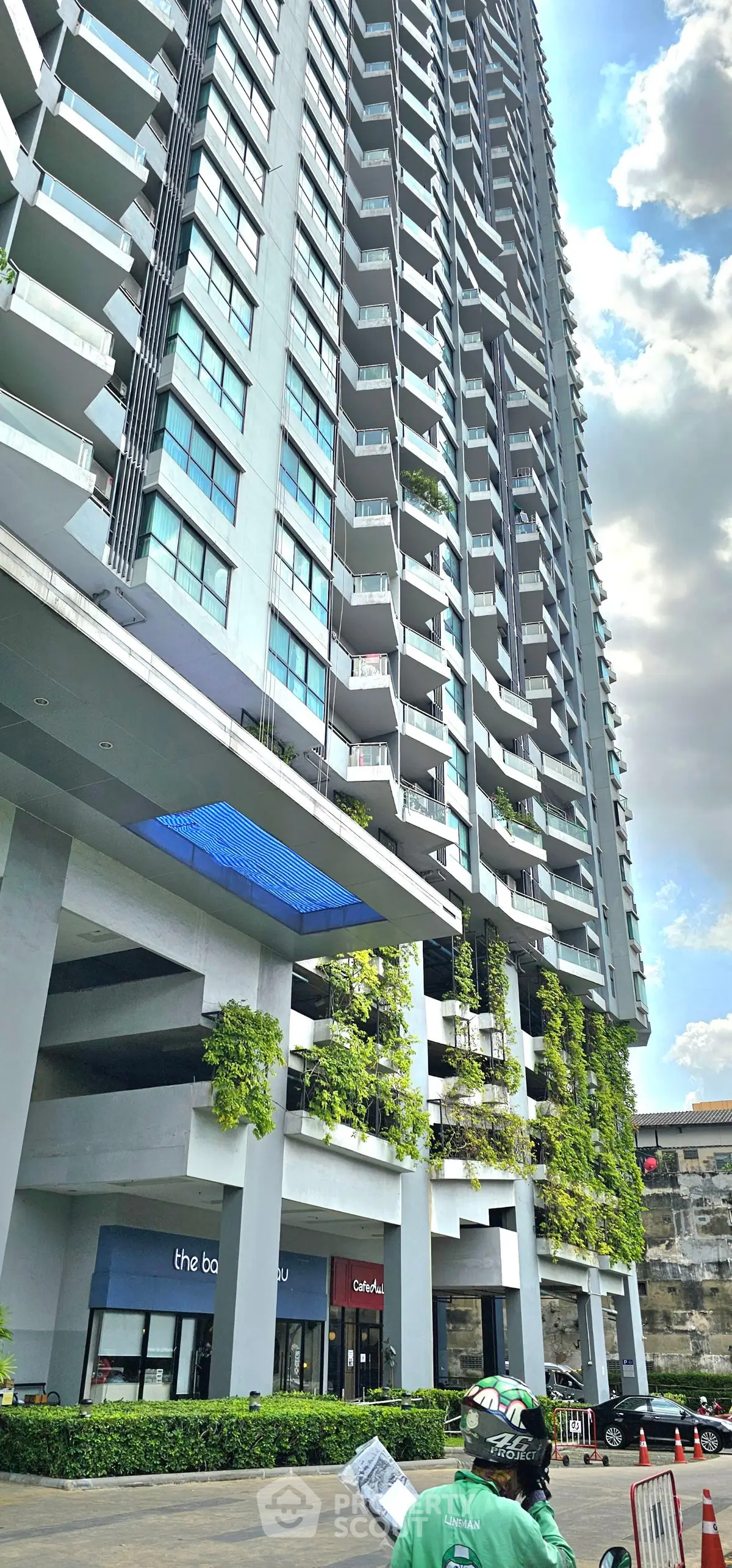 Modern high-rise building with lush greenery and retail spaces at the base, showcasing urban living.