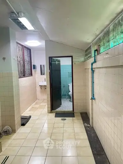 Spacious bathroom with tiled walls and ceiling lighting, featuring a shower and toilet area.